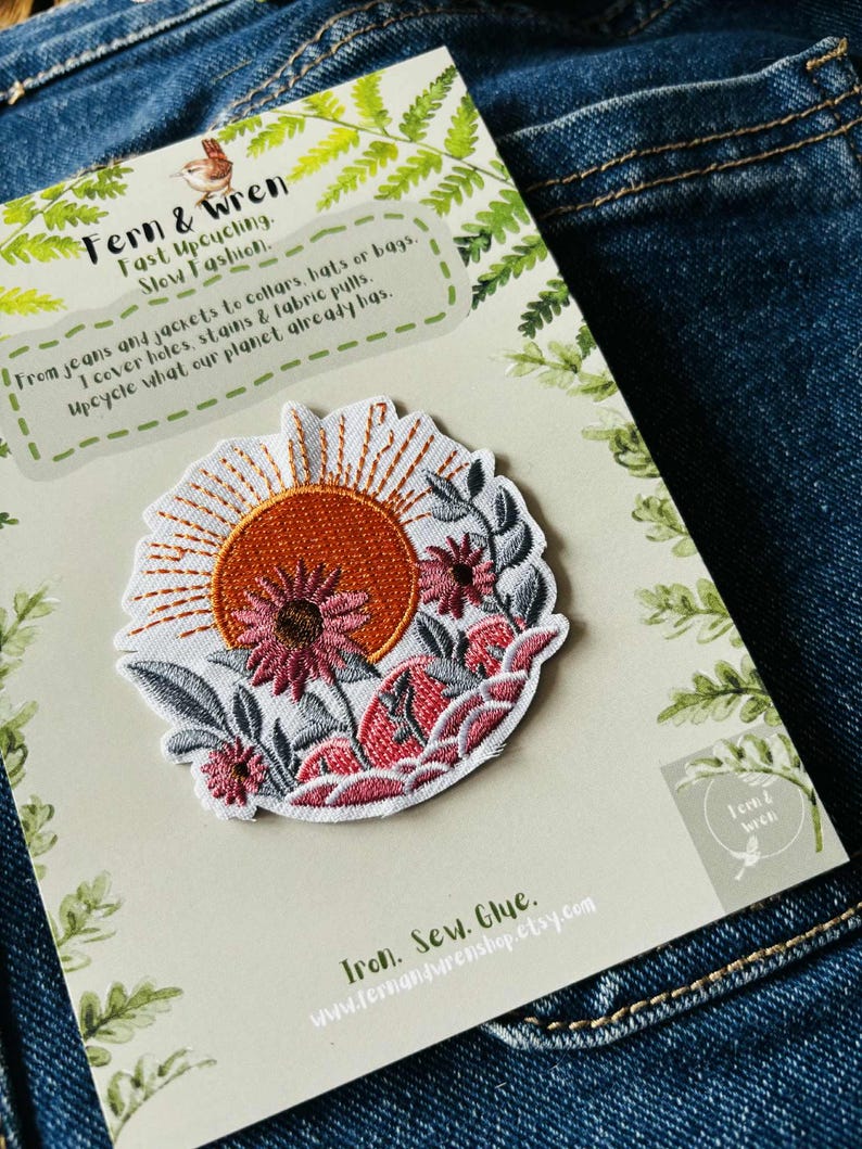 Puede incluir: Parche bordado con dise&ntilde;o de sol y flores en tonos naranja, rosa y blanco. Presentado en una tarjeta con texto: "Fern & Wren, Fast Upcycling, Slow Fashion". Dise&ntilde;ado para cubrir agujeros, manchas y desgarros.
