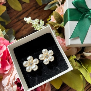 May include: A pair of white pearl flower earrings with a small rhinestone in the centre of each flower. The earrings are in a white gift box with a black velvet lining.