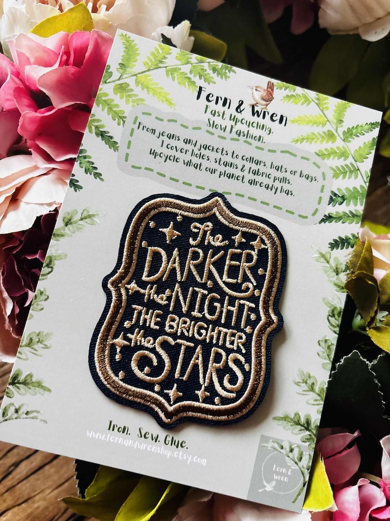 May include: A navy blue embroidered patch with a gold border and gold lettering that reads, The Darker the Night the Brighter the Stars. The patch is attached to a white display card featuring green fern illustrations and brand text.