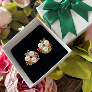 May include: Two gold-tone brooches with white pearls and colorful gemstones. The brooches are in a white gift box with a green ribbon.