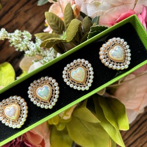 May include: Four heart-shaped pearl and gold-tone brooches in a green velvet box. The brooches have a white iridescent center and are surrounded by a row of pearls.