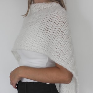 May include: A white, open-weave crochet shawl. The shawl is draped over the shoulders and arms. The garment is made of a soft, textured yarn. The shawl is a neutral color and appears to be handmade.