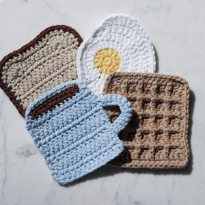 May include: Four crocheted kitchen pot holders shaped like a cup of coffee, a waffle, a fried egg, and a slice of toast.