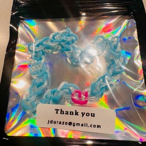 May include: A blue and white rubber band bracelet in a clear plastic bag. The bracelet is in the shape of a heart and has a pink accent. A white label with the words "Thank you" and an email address is visible.