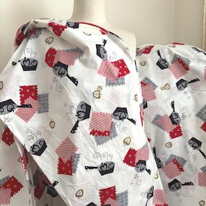May include: White fabric with a repeating pattern of black pots, red and gray patchwork, and gold leaf shapes. The fabric is draped over a mannequin, showcasing the design's potential for sewing projects.