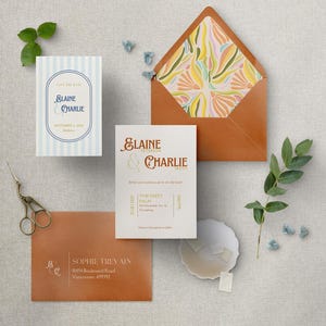 May include: A wedding invitation suite with a light blue and white striped save the date card, a white invitation card with gold text, and a brown envelope with a colorful floral pattern. The invitation card reads "Elaine & Charlie" and includes the date and time of the wedding, as well as the location: "The West Palm, 821 Orangewood Ave. #10, Pasadena". The envelope has a return address label that reads "Sophie Trevain, 10454 Boulevard Road, Vancouver, 659392".