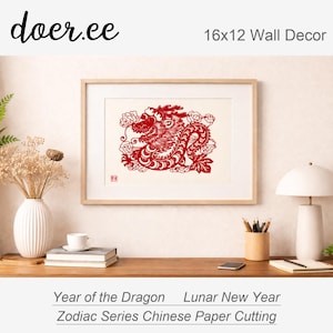 May include: A framed 16x12 inch wall decor piece featuring a red paper-cut dragon design. The artwork is set against a cream background and framed in a light wood. Text at the bottom reads "Year of the Dragon Lunar New Year Zodiac Series Chinese Paper Cutting."