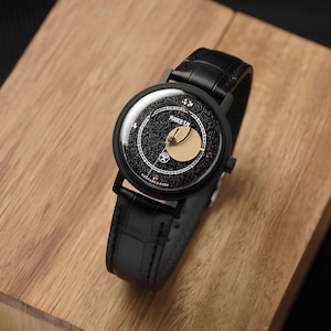 May include: A black wristwatch with a textured black dial, a gold circular accent, and a black leather strap. The dial features the text PAKETA and СДЕЛАНО В СССР in white, with a white minute track and small gold markers at the hour positions.