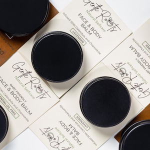 May include: Overhead view of black-lidded jars and product packaging. The packaging is light-coloured with text reading "Gentle Roots Natural Selfcare FACE & BODY BALM" and "DETOX CLAY FACE MASK". The balm is infused with Calendula and Chamomile.