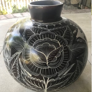 May include: Black ceramic vase with white floral and bird designs. The vase has a round body and a wide mouth.