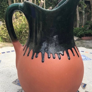 May include: A terracotta pitcher with a black and green glaze. The glaze has a drip effect around the top of the pitcher.