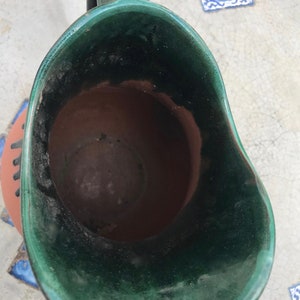 May include: A green glazed ceramic pitcher with a brown clay interior. The pitcher has a wide mouth and a handle.