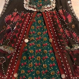 May include: A brown vest with intricate embroidery and beading. The vest is decorated with buttons, safety pins, and white beads. The vest has a green and red floral lining.