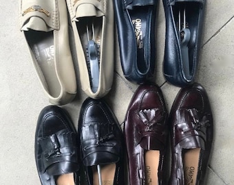 May include: Six pairs of leather loafers in various colors, including beige, navy blue, black, and burgundy. Each pair features a tassel detail and the brand name "Salvatore Ferragamo" embossed on the insole.