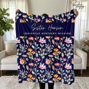 May include: A navy blue blanket with a floral pattern in pink, orange, and yellow. The blanket has the text "Sister Hanson Louisville Kentucky Mission" in white. Scripture references are printed on the blanket.