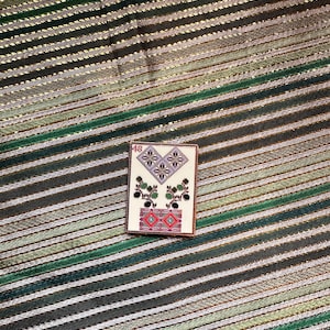 May include: A white card with the number 48 in red in the top left corner. The card features a stylised heart with two green plants on either side. The plants have purple flowers and green leaves. The heart is filled with a pattern of small squares and diamonds in red, white, and blue.