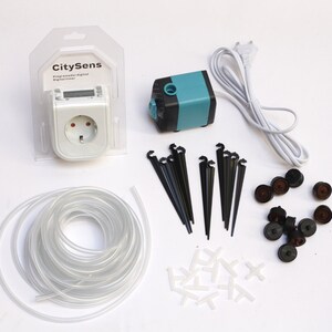 Peut inclure: Un programmateur numérique CitySens blanc avec une prise européenne, une pompe à eau bleue et noire, un tube en plastique transparent, des piques d'irrigation noirs, des connecteurs en T blancs et des émetteurs goutte à goutte bruns et noirs.