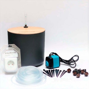 May include: A black and wood self-watering system with a blue pump, clear tubing, and brown drip stakes. The system includes a power adapter with a European plug. The packaging includes the text "CitySens".