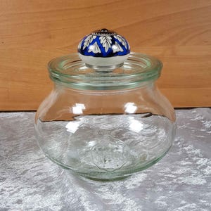 Könnte beinhalten: Ein klares Glasgefäß mit einem blauen und weißen Keramikdeckel. Der Deckel hat ein Blumenmuster.