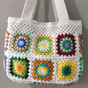 May include: White crochet tote bag with colorful granny square designs. The bag has two straps and is made with a white yarn.