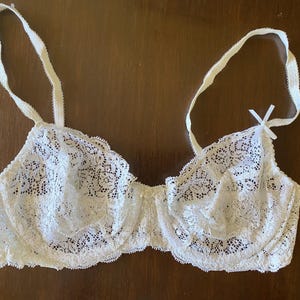May include: Ivory-colored lace bra with adjustable straps and a delicate bow detail. The bra features a floral lace pattern and is designed with underwire support. A classic lingerie piece.