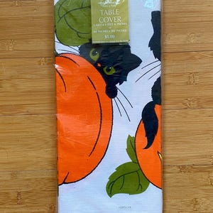 May include: A Halloween-themed table cover in a clear plastic package. The white fabric features orange pumpkins, black cats, and green leaves. The packaging includes the text "TABLE COVER" and measurements of 5 feet x 8 feet 6 inches.