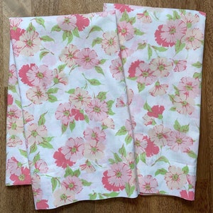 May include: Two white floral patterned bed sheets. The sheets feature a repeating pattern of pink and peach flowers with green leaves. The flowers are in full bloom and scattered across the fabric.