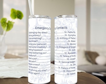 May include: Two white stainless steel tumblers with a straw, featuring a blue floral design and text. One tumbler lists "Emergency Contacts" and the other lists "Emergency Cry" with various questions and saint names.
