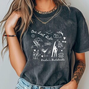 May include: A black t-shirt with a white graphic design that says "One Last Ride" and includes beach-themed illustrations. The text "Kristin's Bachelorette" is also included in the design.