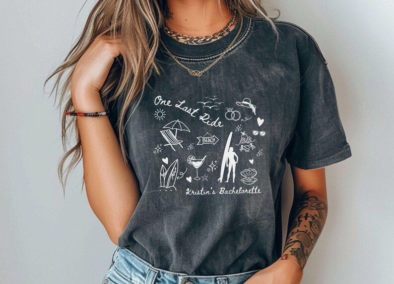May include: A black t-shirt with a white graphic design that says "One Last Ride" and includes beach-themed illustrations. The text "Kristin's Bachelorette" is also included in the design.