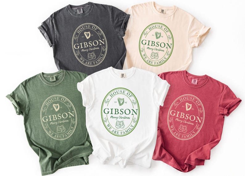 May include: Five t-shirts in various colors: charcoal, cream, green, white, and red. Each shirt features a circular design with the text "HOUSE OF GIBSON Merry Christmas WE ARE FAMILY" in a vintage style. The design includes a harp and two stockings.