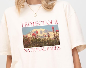 May include: A white t-shirt with the text "PROTECT OUR NATIONAL PARKS" printed in red. The shirt features a vintage-style image of a mountain range with pink wildflowers.