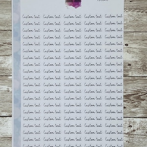 May include: A sheet of clear stickers with the text "Custom text" repeated multiple times in a handwritten font. The stickers are arranged in a grid pattern on a light blue background.