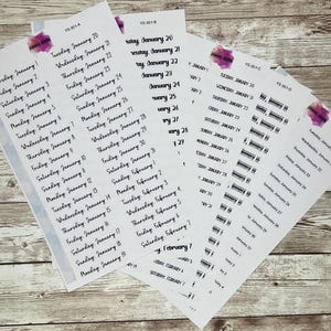 May include: Several white sticker sheets with black text, featuring calendar dates from January and February. The sheets have a watercolor-like purple accent. The dates are arranged in a list format, with days of the week and corresponding dates.