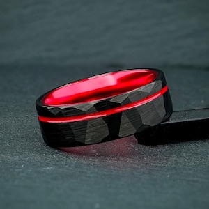 May include: A black ring with a textured surface and a vibrant red interior. The ring features a thin red stripe around the center. The ring is a piece of jewelry.