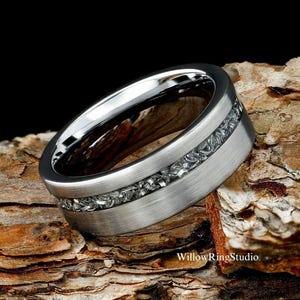 May include: A silver-colored ring with a brushed metal finish and a band of embedded, textured stones. The ring has a polished interior and is set against a dark background and a piece of wood. The text "WillowRingStudio" is visible.