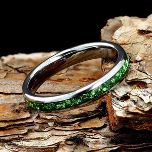May include: A silver ring with a green inlay. The ring is on a piece of wood.