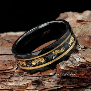 May include: Black tungsten carbide ring with a gold inlay and a textured finish. The ring has a gold band with a black inlay.