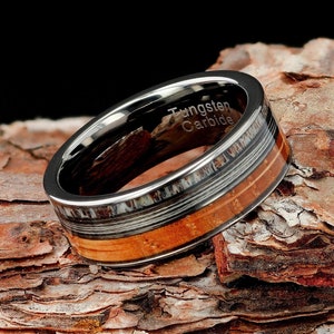 May include: A polished tungsten carbide ring featuring a central inlay of natural wood grain and a textured antler-like material. The interior of the band is clearly engraved with the text Tungsten Carbide in a clean, sans-serif font.