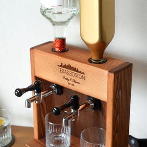 A wooden dispenser with a bottle of alcohol and a gold bottle on top, along with a wooden shelf and a glass.