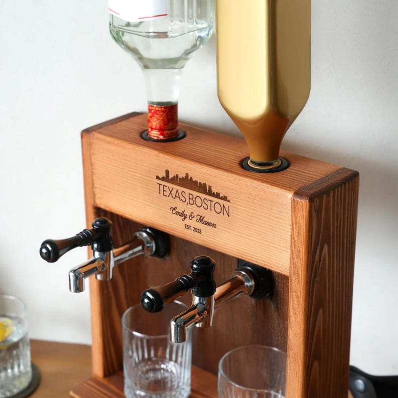 A wooden dispenser with a bottle of alcohol and a gold bottle on top, along with a wooden shelf and a glass.