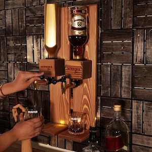 a person holding a glass in front of a wall mounted liquor dispenser