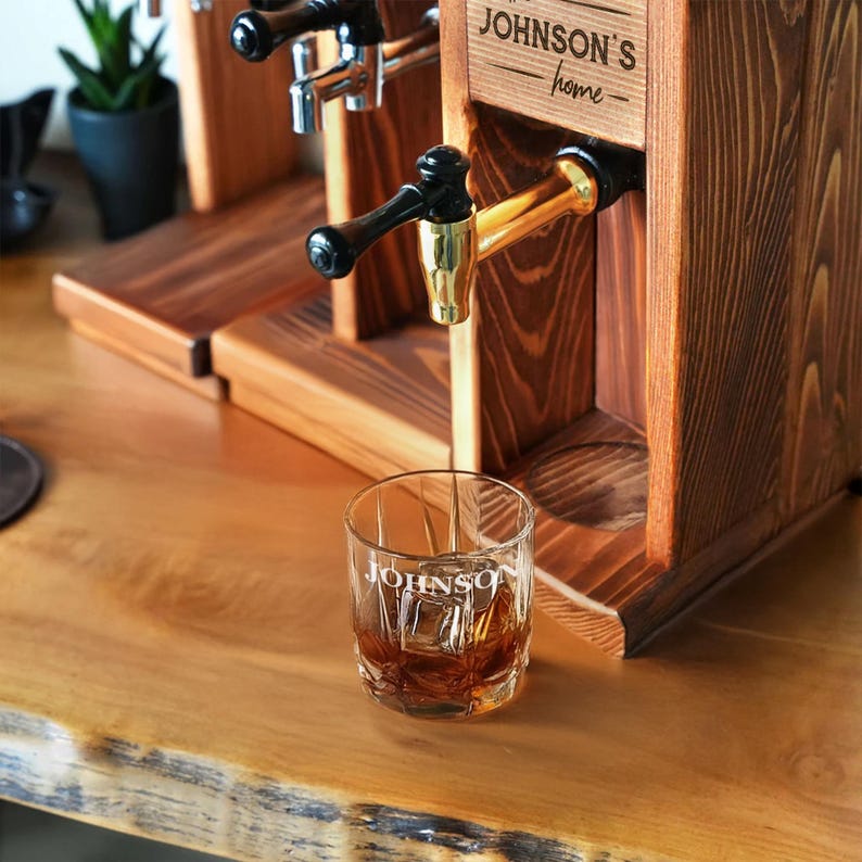 A wooden dispenser with a glass of whiskey, and a potted plant in the background.