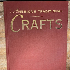 Könnte beinhalten: Ein rotes Hardcover-Buch mit dem Titel "America's Traditional Crafts" in goldenen Lettern.