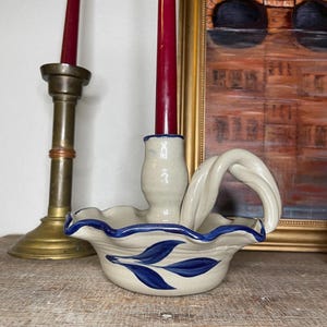Może przedstawiać: Biały ceramiczny świecznik z niebiesko-białym wzorem kwiatowym. Świecznik ma falowany brzeg i skręcony uchwyt. Jest przeznaczony do trzymania jednej świecy.