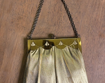 May include: A gold metallic clutch purse with a chain strap. The purse has a scalloped top with a decorative design.