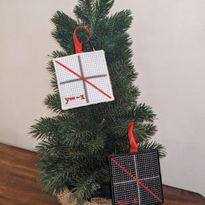 Op de afbeelding: Twee handgemaakte kerstversieringen met een grafiek met een rode lijn die de vergelijking "y=-x" voorstelt. De versieringen zijn wit en zwart met rood touw.