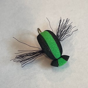 May include: A black and green foam fly fishing lure with black and silver wire wings.