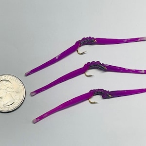May include: Three purple fishing lures with white flecks, each with a gold hook and a silver and purple segmented body.