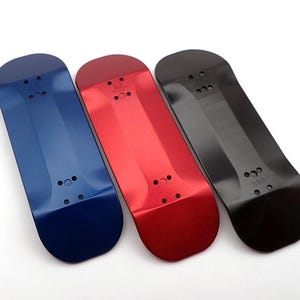 May include: Three fingerboards in blue, red, and black. The fingerboards are made of a smooth, hard material and have a slightly concave shape. Each fingerboard has a small, round hole in the center.